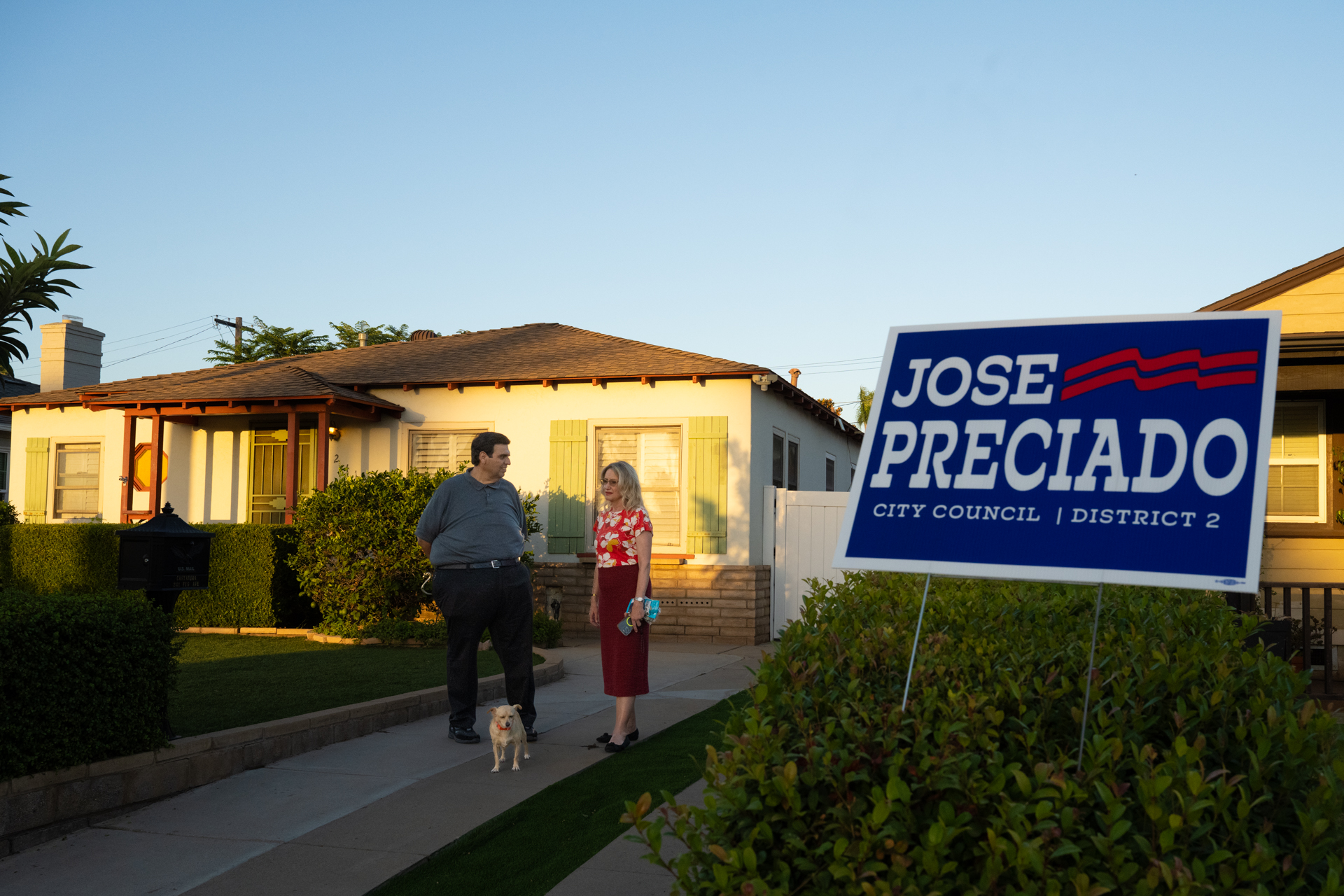 Jose Preciado speaking with a resident beside a campaign yard sign